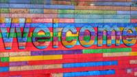 Quelle: unsplash.com / Belinda Fewing, https://unsplash.com/de/fotos/willkommensschild-an-der-mehrfarbigen-holzwand-6wAGwpsXHE0 Bunte Wand mit Welcome